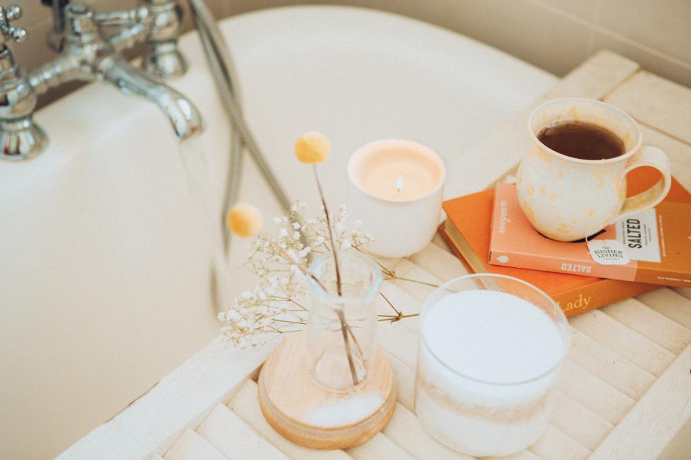 A bath tray with a candle, flowers, a hot drink and books